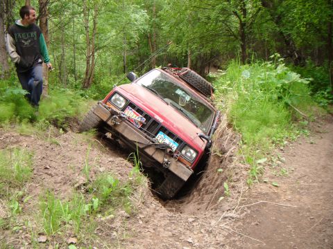 1998 Jeep Cherokee - A red 1998 Jeep Cherokee is stuck in a deep ditch off-road, with a man observing the situation.