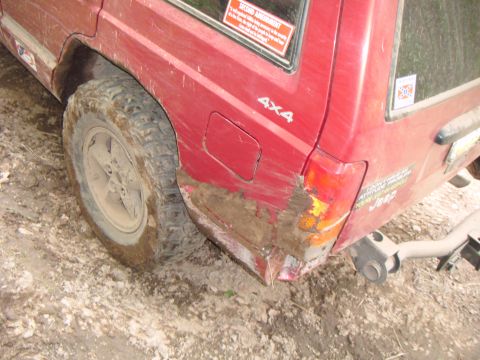 1998 Jeep Cherokee - Rear view of a red 1998 Jeep Cherokee showing mud and damage to the quarter panel and bumper area.