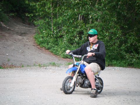 1998 Jeep Cherokee - A person rides a blue dirt bike on a dirt path with trees in the background.