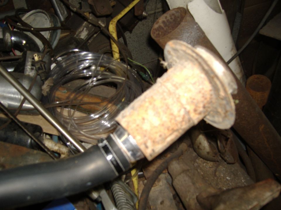 Close-up of a rusty exhaust pipe fitting connected to a black hose, surrounded by various wires and metal parts