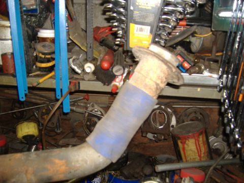 1995 Ford F-150 - Exhaust pipe with blue tape wrap, in a cluttered workshop with various tools and parts.
