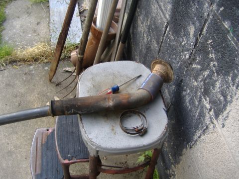 1995 Ford F-150 - A rusty exhaust pipe, a screwdriver, and a hose clamp sit on a stool outdoors.
