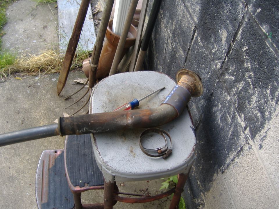 Exhaust pipe with a screwdriver and hose clamp on a stool, leaning against a cinder block wall