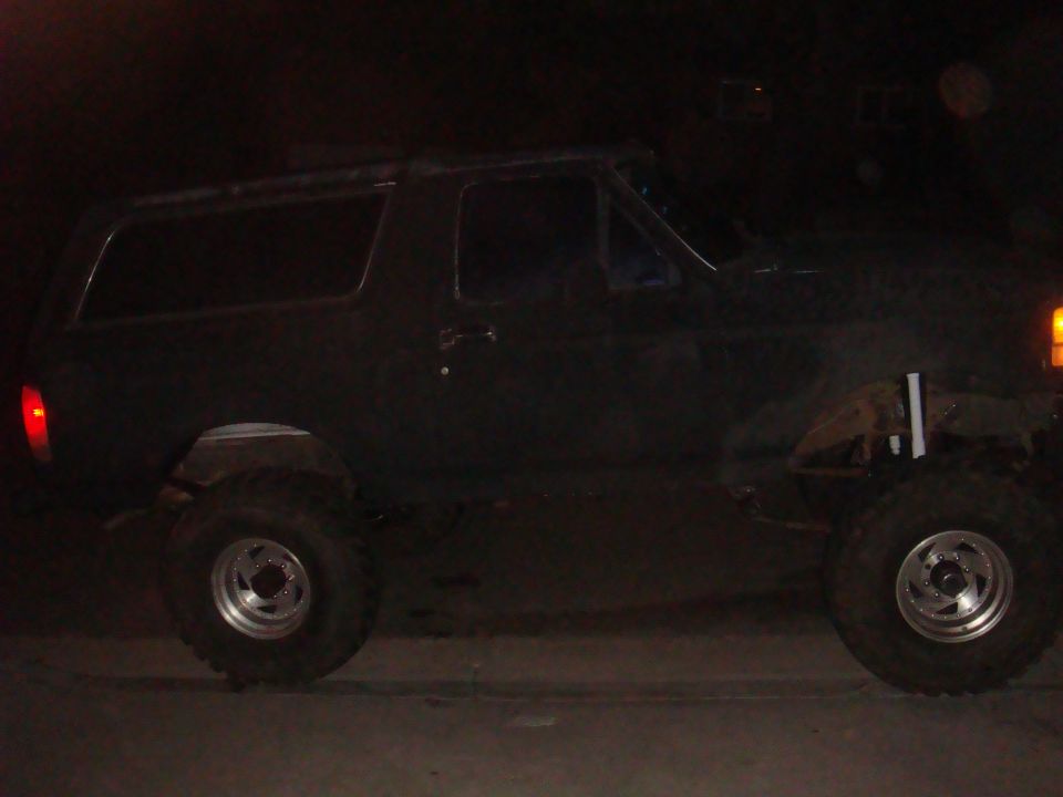 Side view of a dark-colored Ford Bronco, possibly from the early 1980s, with large tires and lifted suspension