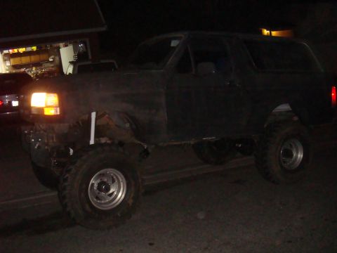 1992 Ford Bronco parked at night, side view. Lifted suspension and large tires are visible