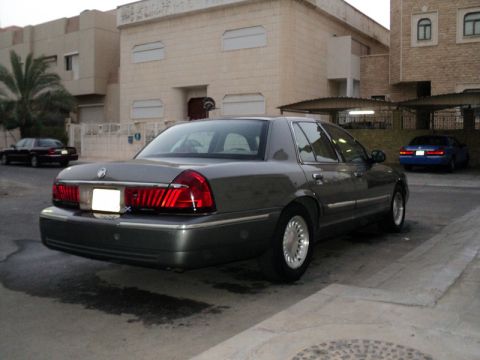 2001 Mercury Grand Marquis - A dark gray Mercury Grand Marquis is parked on a street, with other vehicles and buildings in the background.