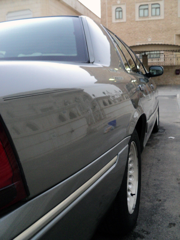 Low side-rear angle of gray-green Mercury sedan showing chrome molding and alloy wheel