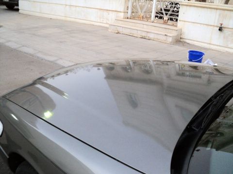 2001 Mercury Grand Marquis - The hood of a silver sedan is shown, reflecting the surroundings. A blue bucket sits on the sidewalk nearby.