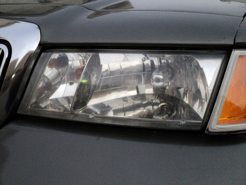 Clear composite headlight with chrome reflector and amber corner marker on a dark gray sedan