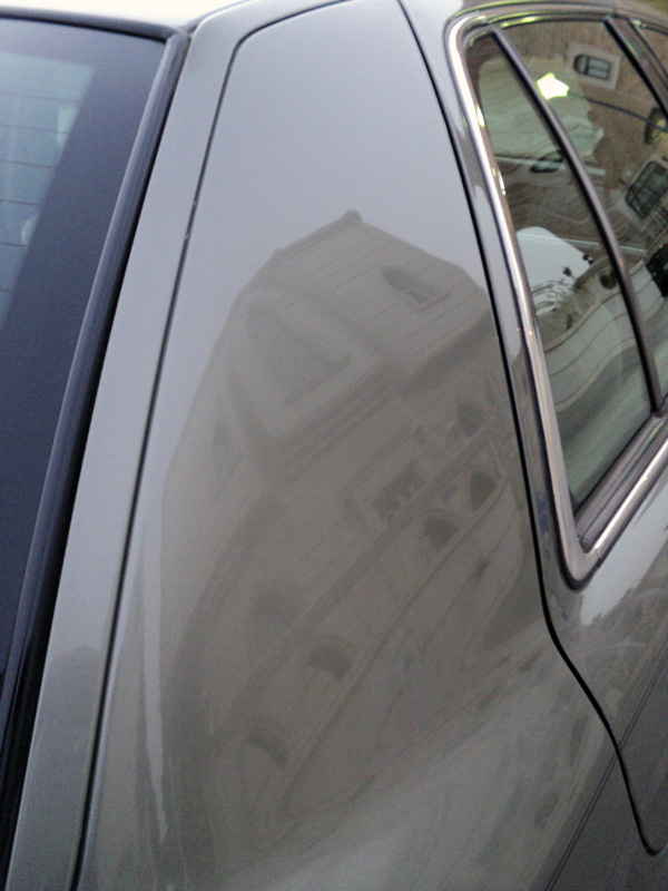 Building reflected in the polished silver rear quarter panel and chrome window trim of a sedan
