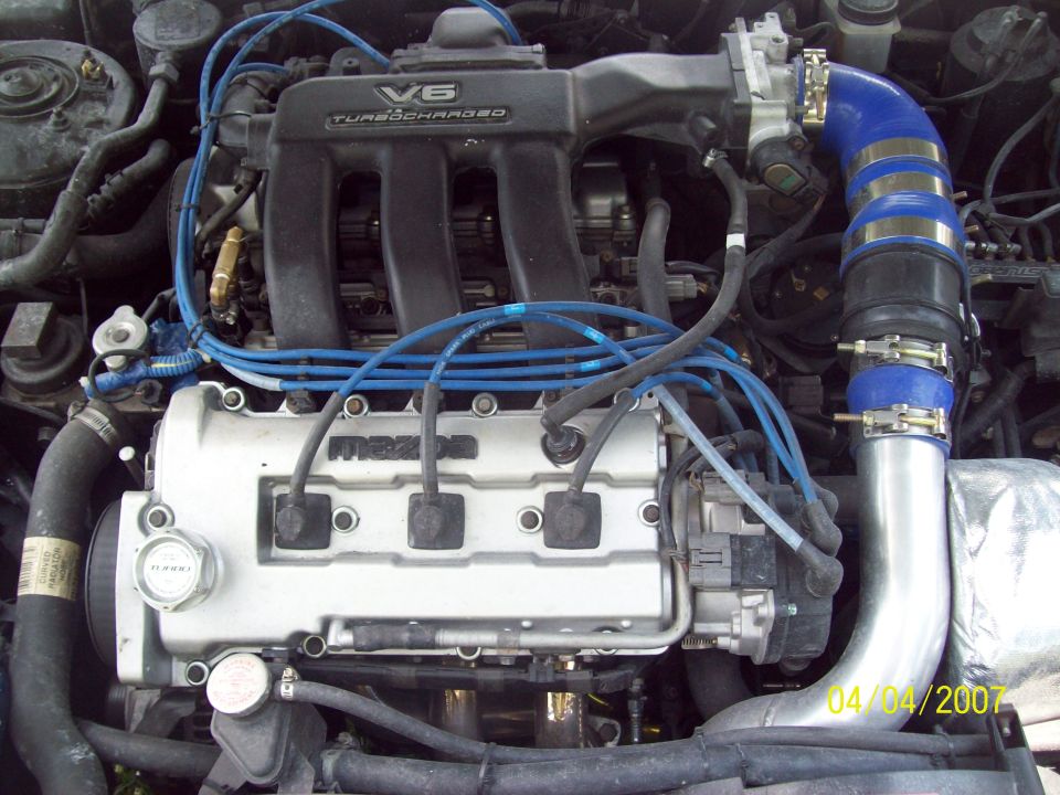 Mazda V6 turbocharged engine bay with blue plug wires and polished charge pipe