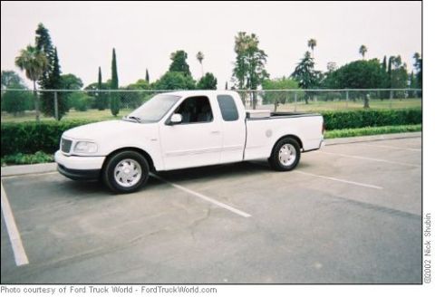 1988 Ford Bronco - This white Ford F-150 pickup truck is parked in a lot with trees in the background.