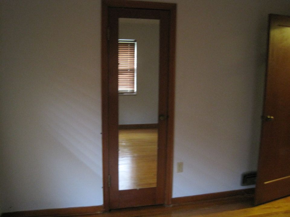 Interior doorway with a mirrored panel reflecting a window and wooden floor