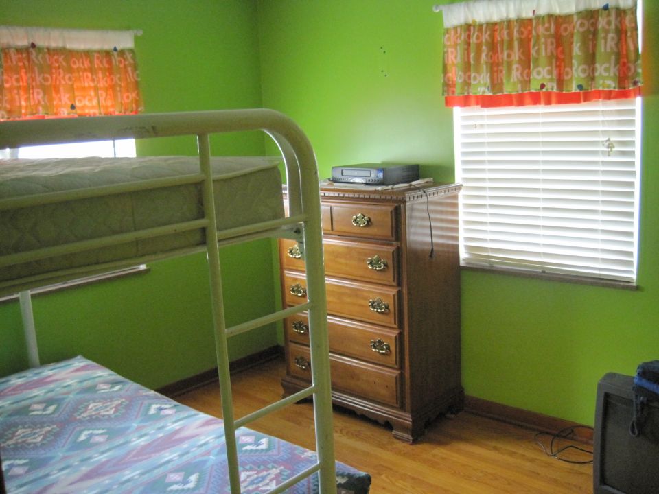 Bunk bed with mattress and patterned bedding next to a wooden dresser with a VCR on top