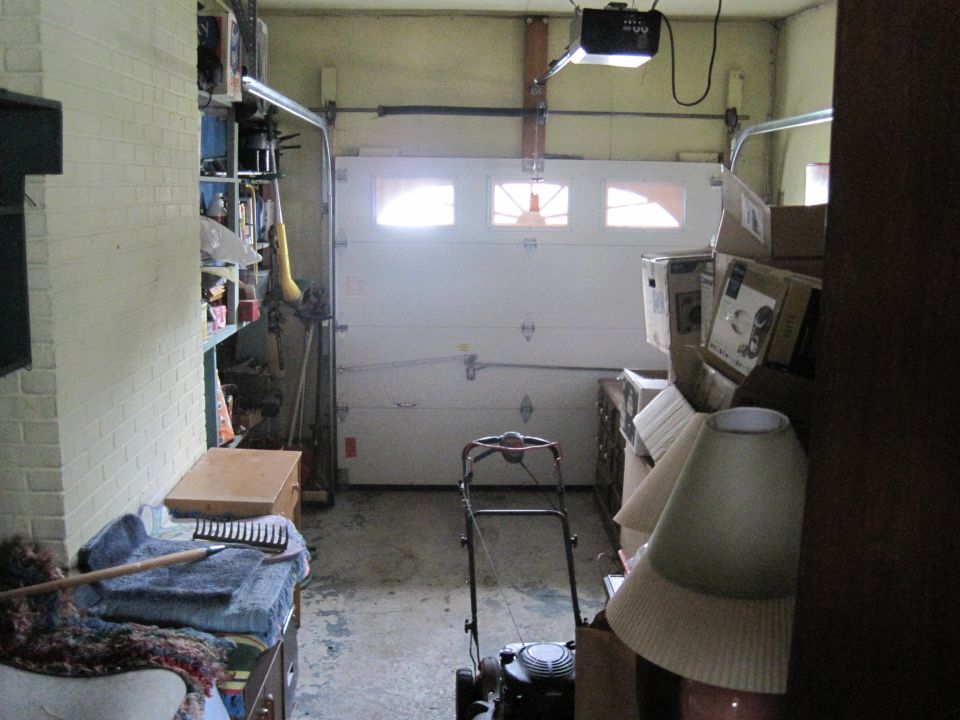 Garage interior with a lawn mower in the center, shelves with items on the left, and boxes stacked on the right