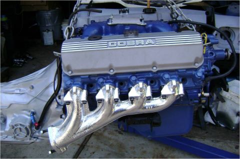 1972 Ford Ranchero - Engine with blue block, Cobra valve covers, and chrome headers, suspended by chains.