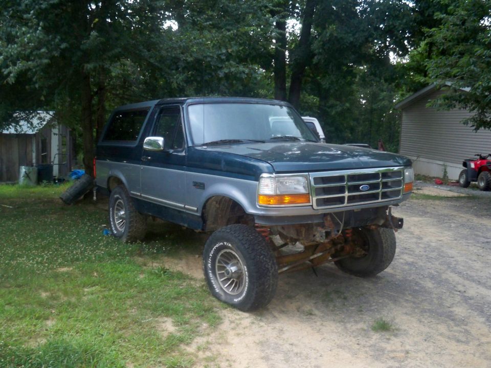 Blue and silver Ford Bronco with lifted suspension and missing front bumper