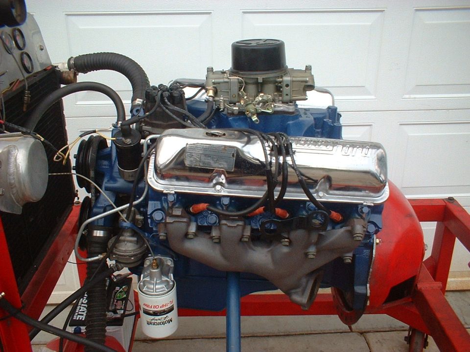 Blue V8 engine with chrome valve covers and a carburetor, mounted on a red stand