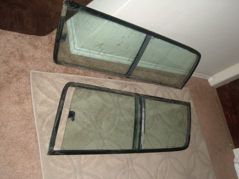 1988 Ford Bronco - Two removed door window assemblies stood on a carpet and area rug indoors, each with a black-painted steel frame, fixed vent section and fu…
