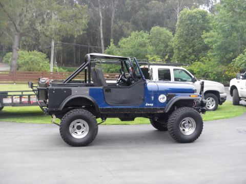 1991 Ford Bronco - A blue Jeep CJ-7 is parked next to two white pickup trucks, with a trailer hitched to the Jeep's rear.