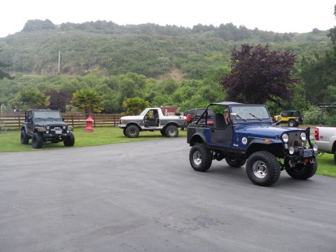 1991 Ford Bronco - A collection of off-road vehicles, including Jeeps and a Ford truck, are parked on an asphalt surface.