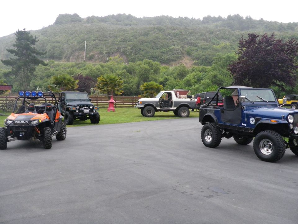 Several off-road vehicles parked in a lot, including a blue Jeep, a white Ford truck, and an orange ATV