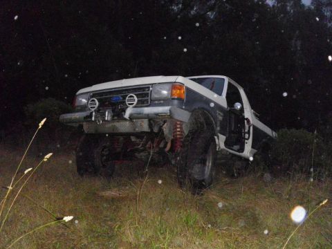 1991 Ford Bronco - This lifted 1991 Ford Bronco features off-road tires and a two-tone paint scheme, seen in a grassy, wooded area at night.