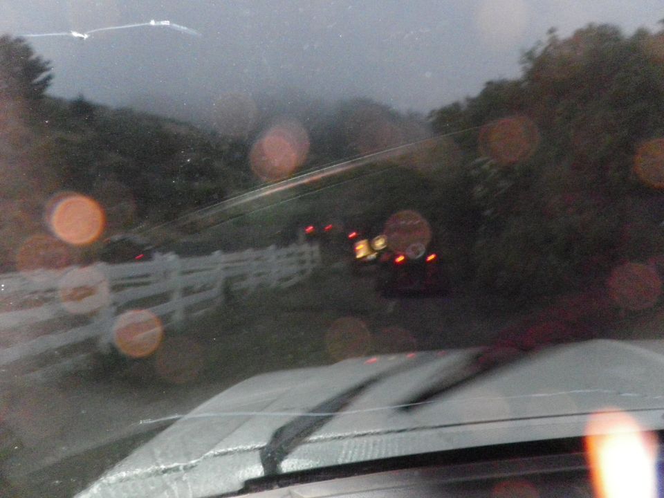Interior view of a vehicle looking out the windshield at a road with a white fence and distant traffic