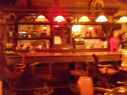 1991 Ford Bronco - The dimly lit interior of a bar features a wooden counter and stools, with shelves filled with bottles in the background.