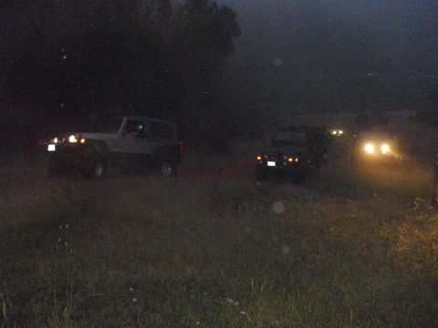 1991 Ford Bronco - Multiple SUVs navigate a dark, unpaved road at night, their headlights cutting through the gloom.