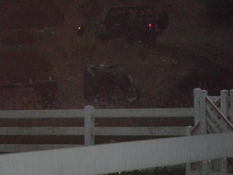 1991 Ford Bronco - Two vehicles are visible on a hillside, one of which appears to be overturned, with a white fence in the foreground.