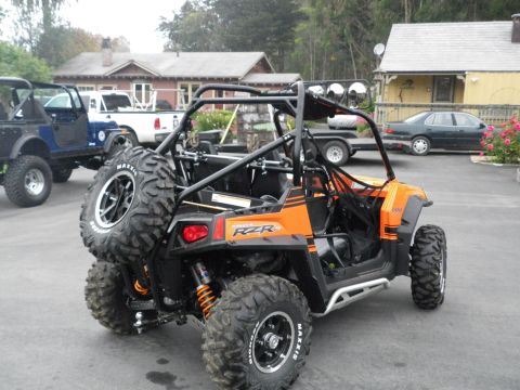 1991 Ford Bronco - An orange side-by-side ATV is parked outdoors with a spare tire on the back. The text "RZR" is visible on the vehicle's body.