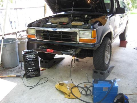 1991 Ford Explorer - A 1991 Ford Explorer is shown with its hood open, elevated on ramps, and surrounded by welding equipment, indicating ongoing maintenance or…