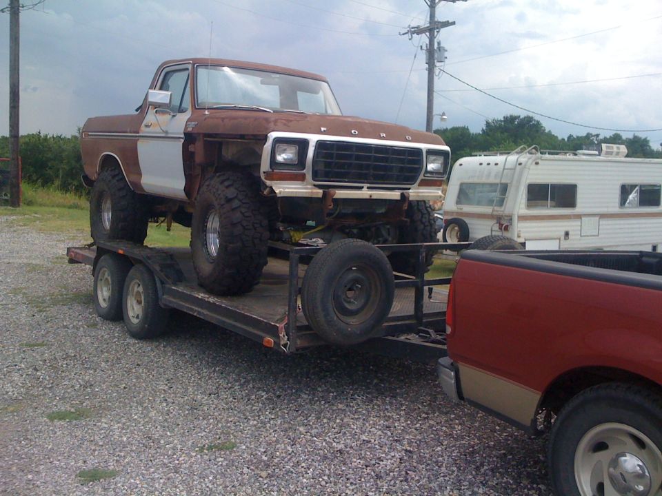 1978 Ford Bronco on trailer, rusty brown and white, lifted with large tires, front end visible