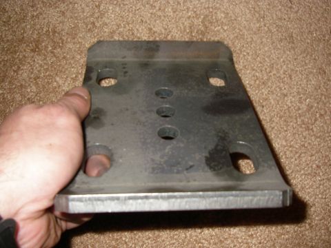 1990 Ford Bronco - A hand holds a metal bracket with several holes drilled into it.