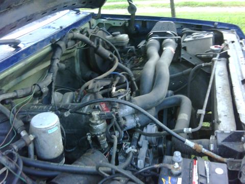 1991 Ford Bronco - Close-up view of a vehicle's engine bay, showing hoses, wiring, and an air filter.