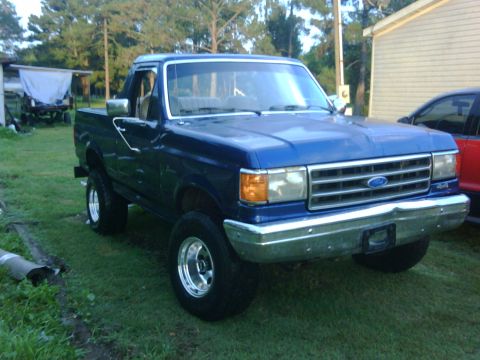 1991 Ford Bronco - This blue pickup truck has a chrome grille and is parked outside on a grassy area.