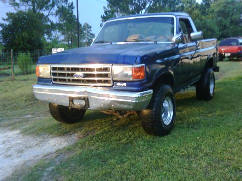 1991 Ford Bronco - A blue pickup truck is parked on a grassy area with a dirt path in front.