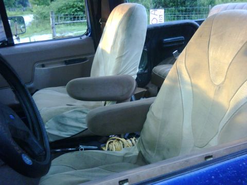 1991 Ford Bronco - The interior of a vehicle shows tan cloth seats and armrests, with a yellow rope on the floor.