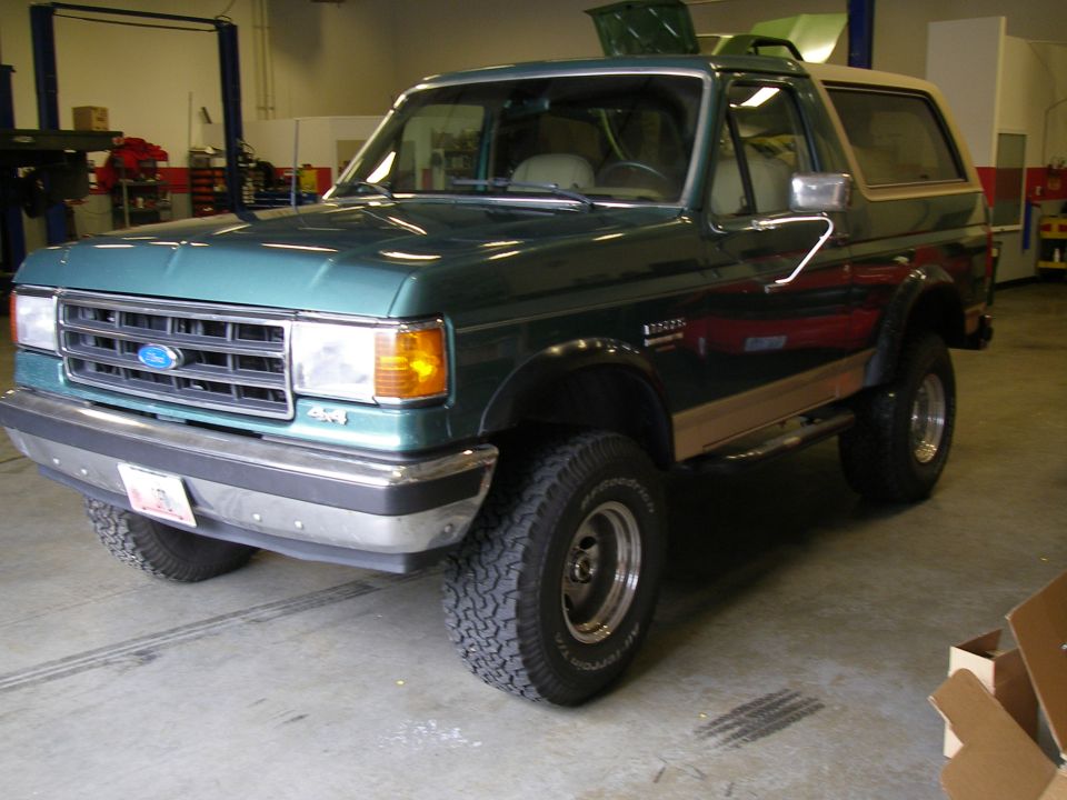 Lifted green and tan Ford Bronco on BFGoodrich All-Terrain tires parked inside a shop