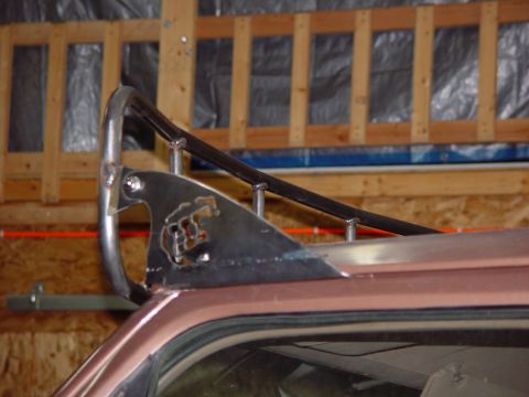 1993 Ford Bronco - Close-up of a shop-built bare steel roof rack end mounted along the roof edge of a pink-primered vehicle, with a curved tube hoop, a plasma…