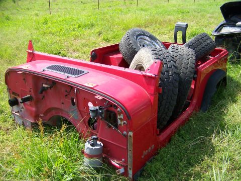 1992 Jeep YJ - The body of a red Jeep is shown with several spare tires loaded in the rear cargo area.