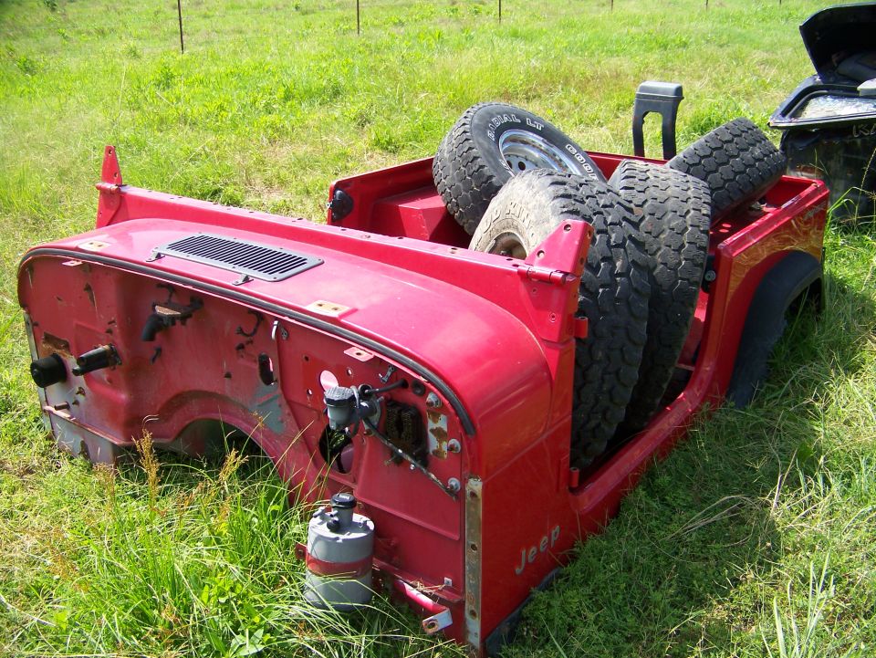 red Jeep tub with spare tires in the bed, parked in grass