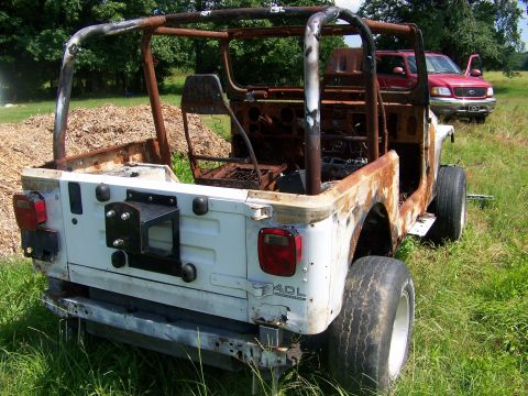 1992 Jeep YJ - A heavily rusted and damaged white Jeep Wrangler is seen in a grassy field, with another vehicle in the background.