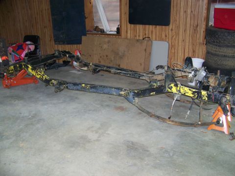 1992 Jeep YJ - The bare frame of a vehicle is supported by jack stands in a garage setting.
