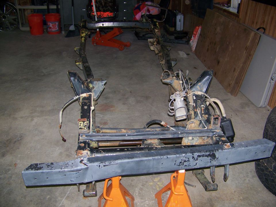Stripped 4x4 frame on orange jack stands in a garage, rear view