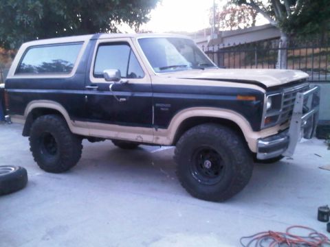 1986 Ford Bronco - This two-tone Ford Bronco sits on a concrete surface with a spare tire nearby.