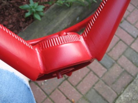 1966 Ford F-100 - Close-up of a repainted glossy red steering wheel held outdoors, focused on the ribbed center hub cover and the finger-grip ridges along th…