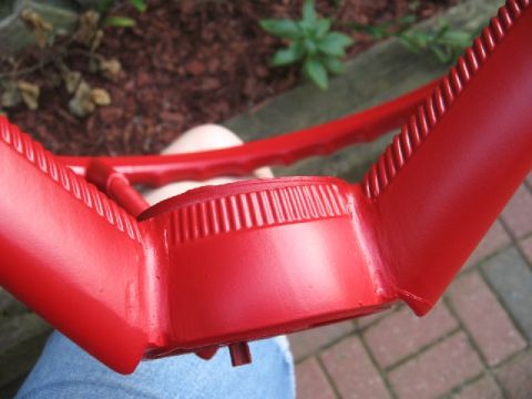 1966 Ford F-100 - Close-up of a freshly painted bright red steering wheel held over someone's lap outdoors, showing the ribbed center hub cover and finger-gr…