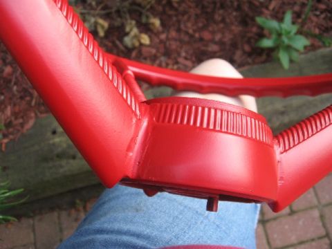 1966 Ford F-100 - A red steering wheel is shown from an interior perspective, with a person's legs in the foreground.